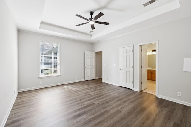 unfurnished bedroom featuring a raised ceiling, dark wood-type flooring, ensuite bath, baseboards, and crown molding