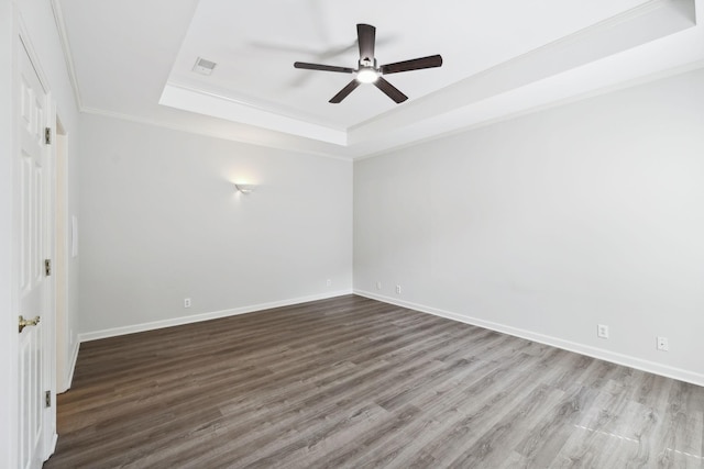 empty room with a tray ceiling, a ceiling fan, wood finished floors, baseboards, and crown molding