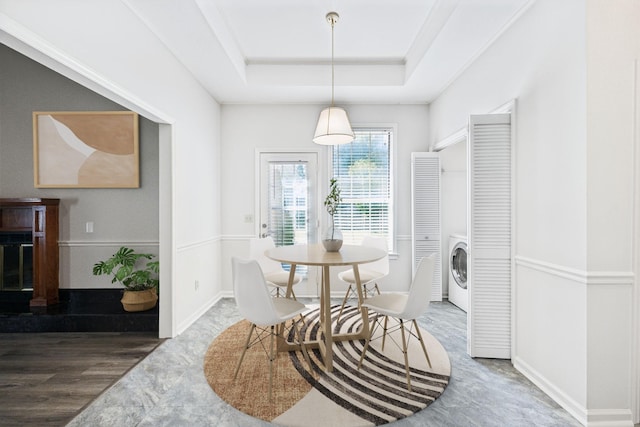 dining room with washer / clothes dryer, a tray ceiling, baseboards, and wood finished floors