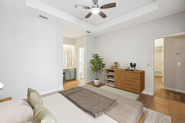 bedroom featuring tile patterned flooring, a tray ceiling, baseboards, and ensuite bath