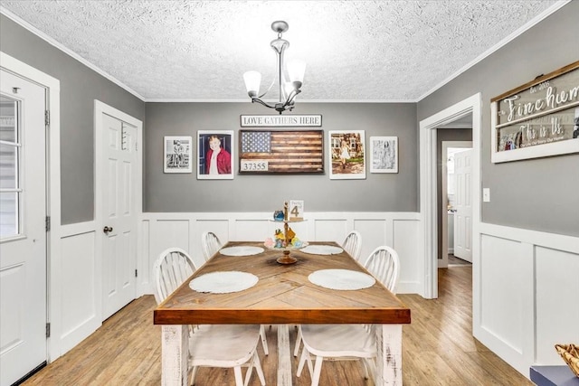 dining area with light wood finished floors, a chandelier, crown molding, a textured ceiling, and a decorative wall