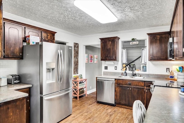 kitchen with stainless steel appliances, a sink, dark brown cabinets, a textured ceiling, and ornamental molding