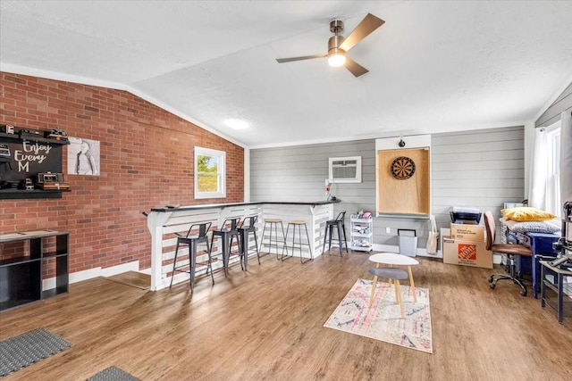 interior space featuring a ceiling fan, plenty of natural light, lofted ceiling, wood finished floors, and brick wall