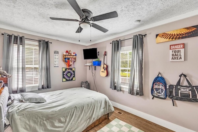 bedroom featuring baseboards, wood finished floors, ceiling fan, and a textured ceiling
