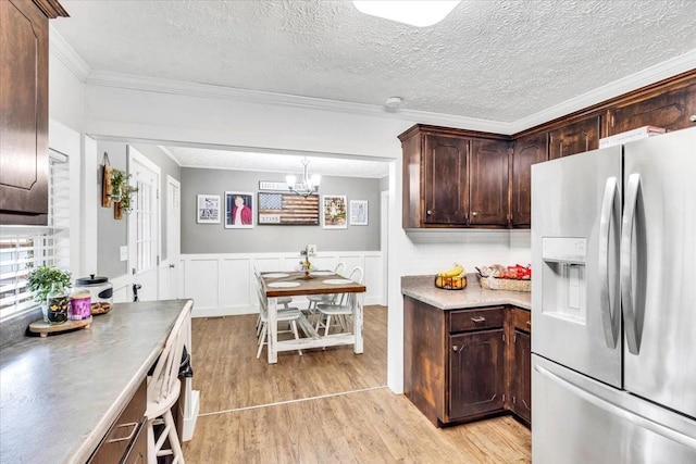 kitchen with stainless steel fridge, light wood finished floors, dark brown cabinetry, a chandelier, and a wainscoted wall