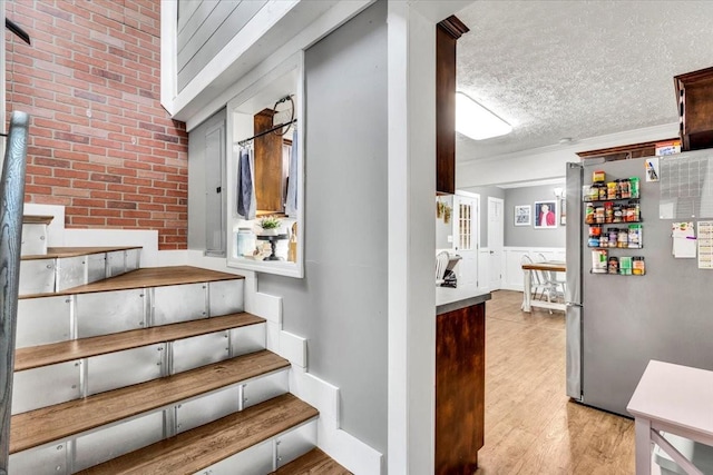 staircase featuring wood finished floors, brick wall, a textured ceiling, and wainscoting
