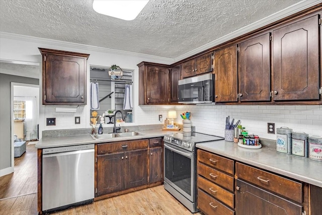 kitchen with stainless steel appliances, light wood-style floors, a sink, decorative backsplash, and a textured ceiling