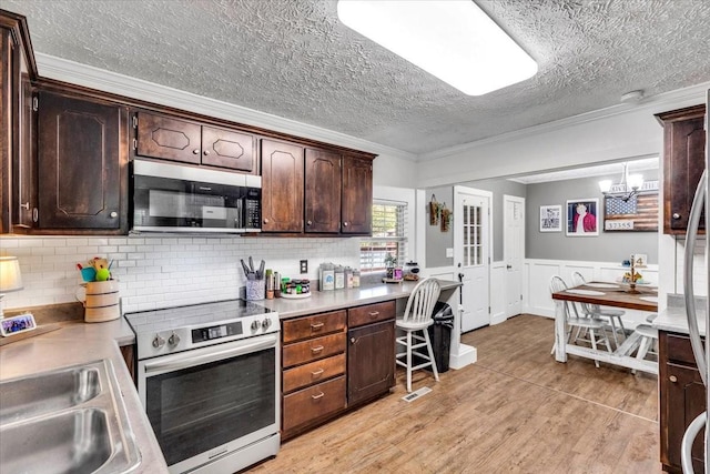 kitchen with appliances with stainless steel finishes, light countertops, a textured ceiling, dark brown cabinets, and light wood-style flooring