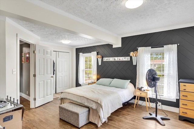 bedroom with a textured ceiling, wood finished floors, beam ceiling, a closet, and baseboards