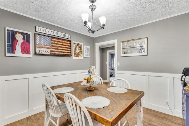 dining space featuring a decorative wall, a chandelier, light wood-type flooring, and crown molding