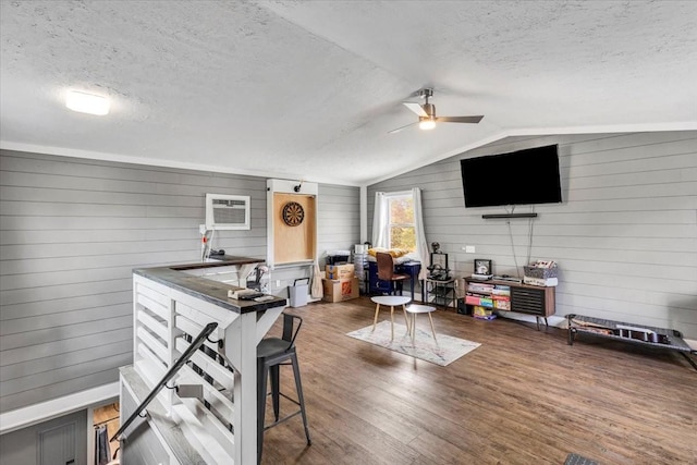 living room featuring a textured ceiling, a ceiling fan, an AC wall unit, vaulted ceiling, and wood finished floors