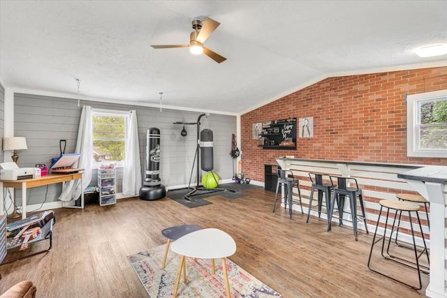 rec room featuring a ceiling fan, healthy amount of natural light, wood finished floors, lofted ceiling, and brick wall