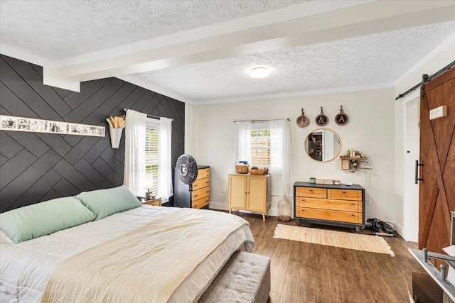 bedroom featuring a barn door, a textured ceiling, an accent wall, wood finished floors, and ornamental molding