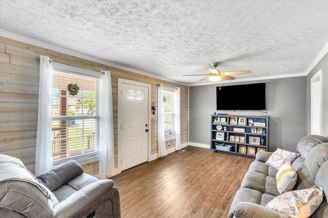 living area featuring ornamental molding, a ceiling fan, wood finished floors, a textured ceiling, and baseboards