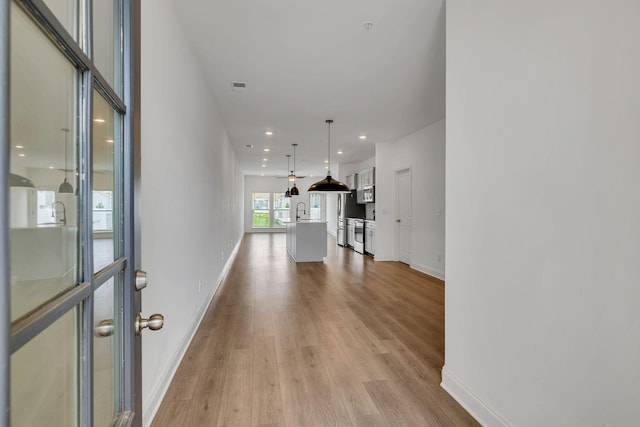 hallway featuring light wood-type flooring, baseboards, and recessed lighting