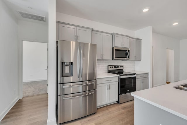 kitchen featuring appliances with stainless steel finishes, gray cabinetry, light countertops, light wood-style flooring, and recessed lighting