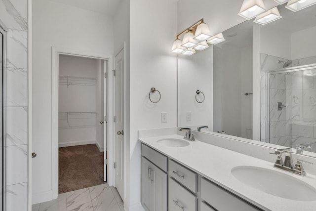 bathroom with marble look tile flooring, a shower stall, double vanity, a walk in closet, and baseboards