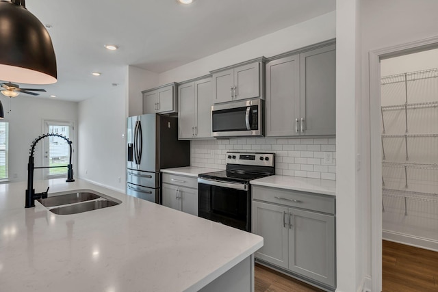 kitchen featuring stainless steel appliances, gray cabinets, a sink, backsplash, and recessed lighting