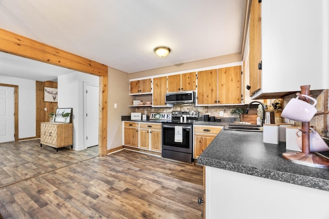kitchen featuring appliances with stainless steel finishes, dark countertops, dark wood finished floors, a sink, and tasteful backsplash