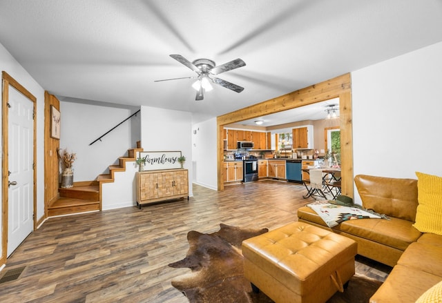 living room featuring dark wood-style flooring, ceiling fan, stairway, and baseboards