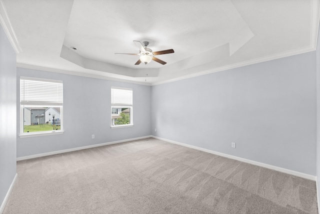 carpeted spare room with a tray ceiling, ceiling fan, baseboards, and ornamental molding