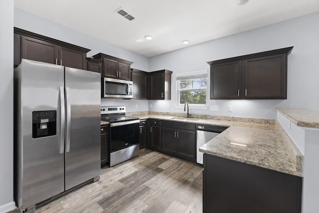 kitchen featuring stainless steel appliances, a sink, light wood-style floors, a peninsula, and dark brown cabinets