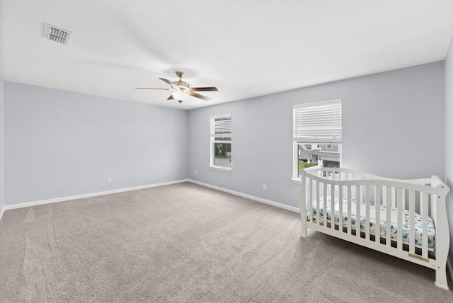unfurnished bedroom featuring carpet, baseboards, ceiling fan, and a crib