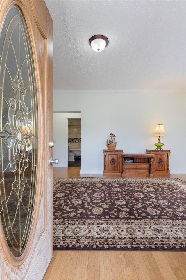 entrance foyer featuring ornamental molding, wood finished floors, a textured ceiling, and baseboards