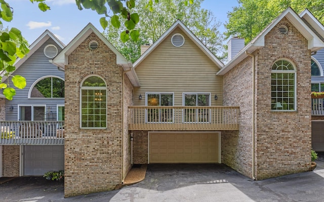 traditional-style house with a garage, asphalt driveway, brick siding, and a balcony