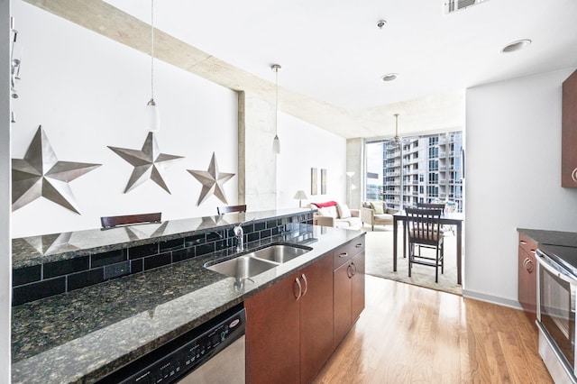 kitchen with a sink, stainless steel appliances, light wood-type flooring, pendant lighting, and dark stone counters