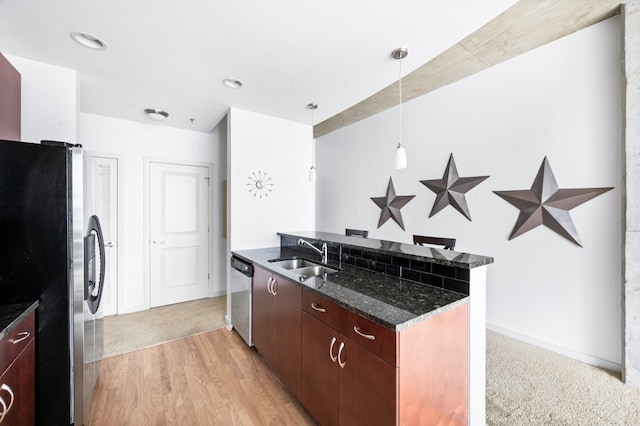 kitchen with stainless steel appliances, a sink, dark stone counters, pendant lighting, and light wood finished floors