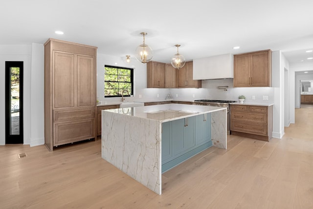 kitchen with a sink, light wood-type flooring, a center island, recessed lighting, and light stone counters