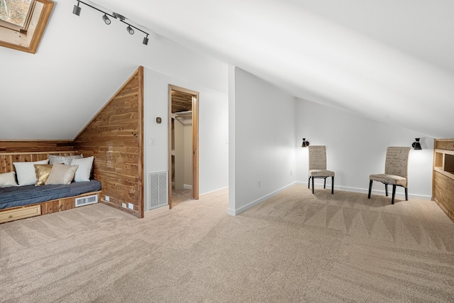 bedroom with vaulted ceiling, wood walls, track lighting, carpet, and a skylight