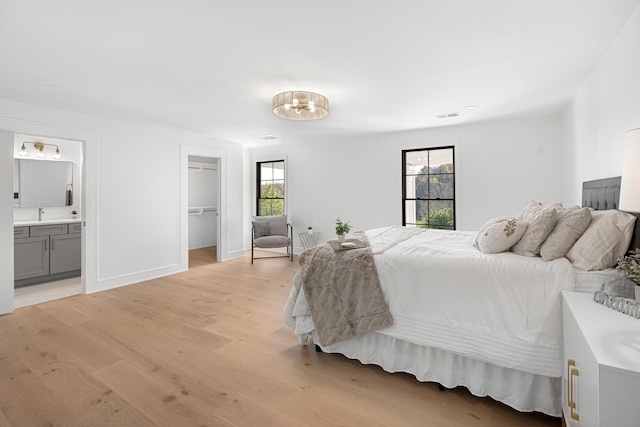 bedroom featuring multiple windows, light wood-style flooring, a chandelier, and a spacious closet