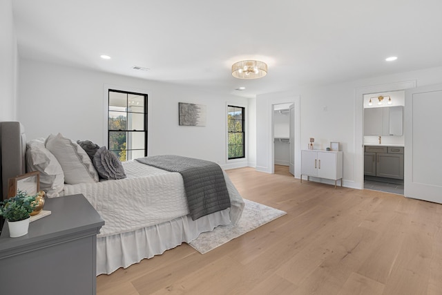 bedroom with light wood-type flooring, recessed lighting, a walk in closet, connected bathroom, and baseboards