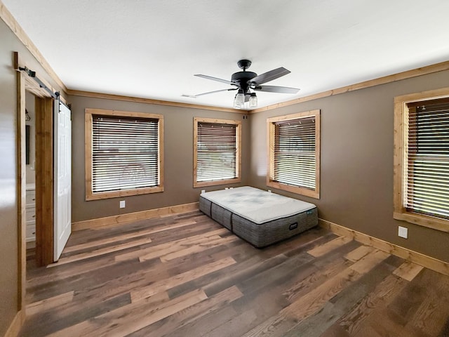 bedroom with wood finished floors, a barn door, baseboards, a ceiling fan, and crown molding