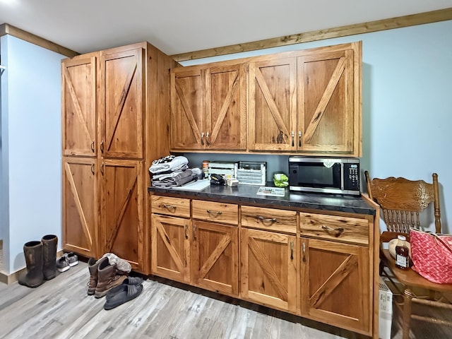 kitchen with stainless steel microwave, dark countertops, wood finished floors, and brown cabinets