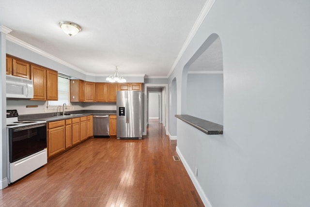 kitchen with appliances with stainless steel finishes, a sink, arched walkways, dark wood finished floors, and a chandelier