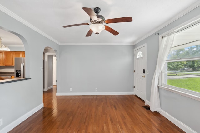unfurnished living room with arched walkways, wood finished floors, a ceiling fan, baseboards, and crown molding