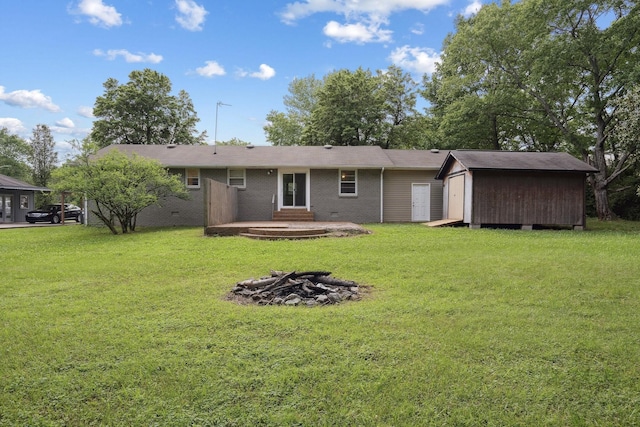 rear view of property featuring a fire pit, a shed, a lawn, and an outdoor structure