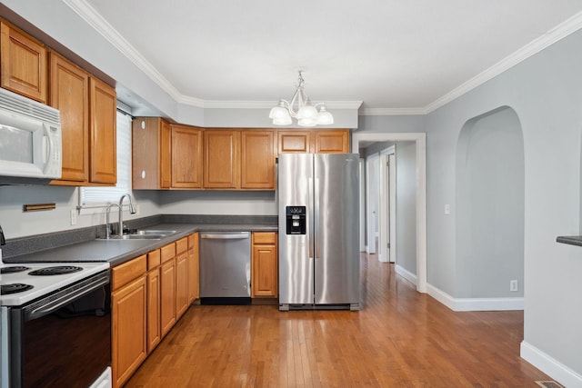 kitchen with appliances with stainless steel finishes, a sink, dark countertops, wood finished floors, and a chandelier