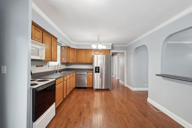 kitchen with stainless steel appliances, a sink, wood finished floors, baseboards, and dark countertops