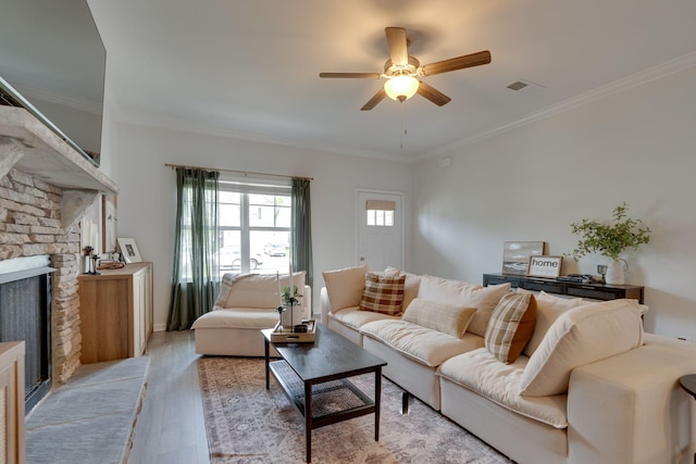 living room with ceiling fan, crown molding, light wood finished floors, and a stone fireplace