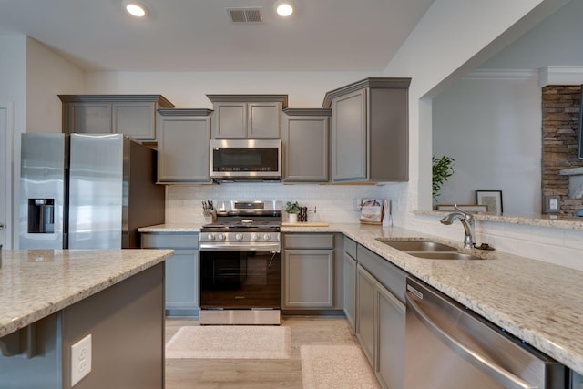 kitchen featuring appliances with stainless steel finishes, a sink, gray cabinets, backsplash, and ornamental molding