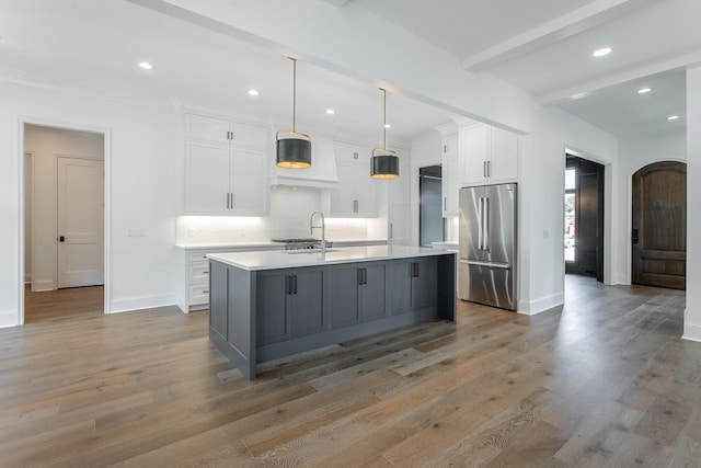 kitchen featuring high quality fridge, a sink, light countertops, white cabinetry, and a kitchen island with sink