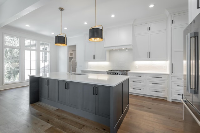 kitchen featuring a sink, high end fridge, backsplash, a center island with sink, and light countertops