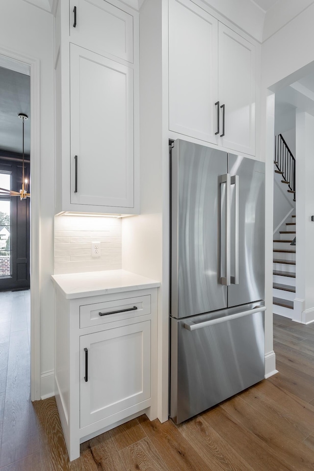kitchen with stainless steel fridge, wood finished floors, white cabinetry, a chandelier, and light countertops