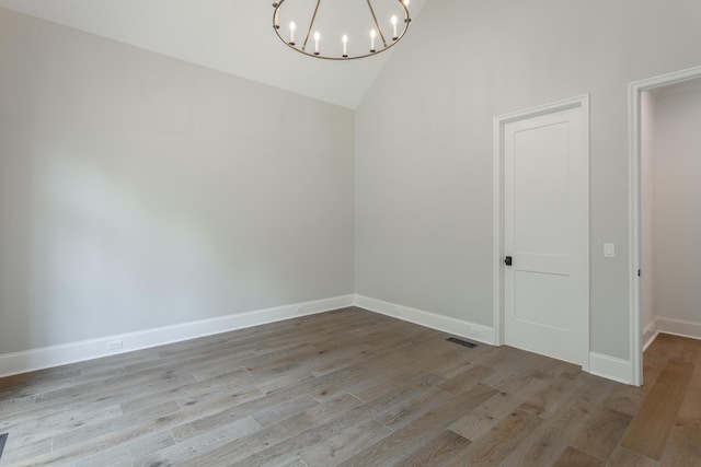 spare room featuring a chandelier, wood finished floors, high vaulted ceiling, and baseboards