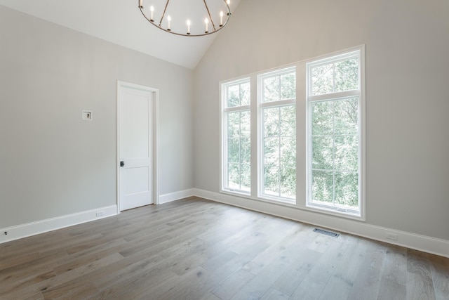 spare room featuring a chandelier, baseboards, wood finished floors, and high vaulted ceiling