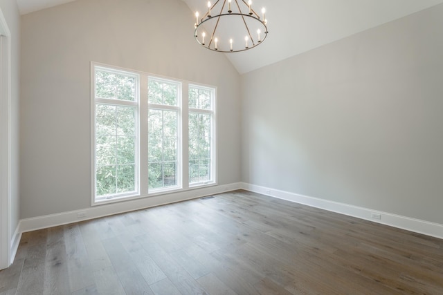 empty room featuring vaulted ceiling, a chandelier, wood finished floors, and baseboards